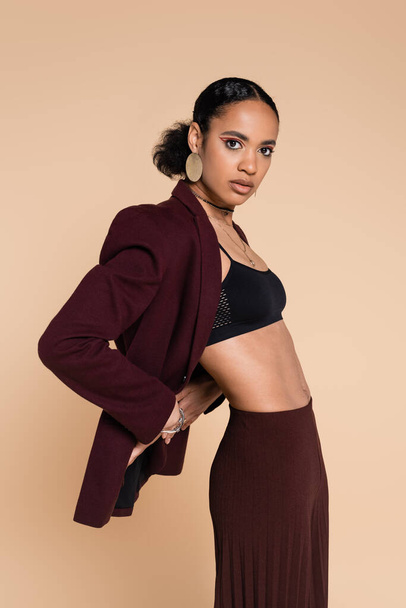 young african american woman in crop top and stylish maroon suit posing isolated on beige  - Valokuva, kuva