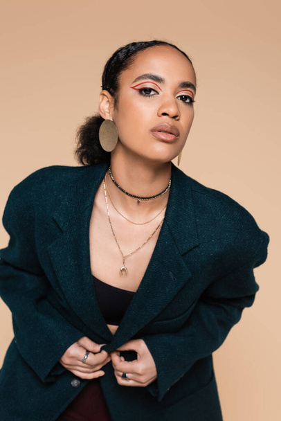 young african american model with makeup posing in dark blue woolen blazer isolated on beige  - Foto, Imagem