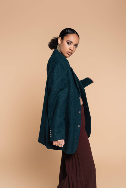 young african american model in dark blue oversized blazer posing isolated on beige  - 写真・画像