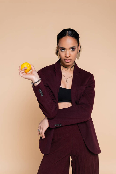african american woman in burgundy blazer posing with fresh lemon isolated on beige  - Photo, Image