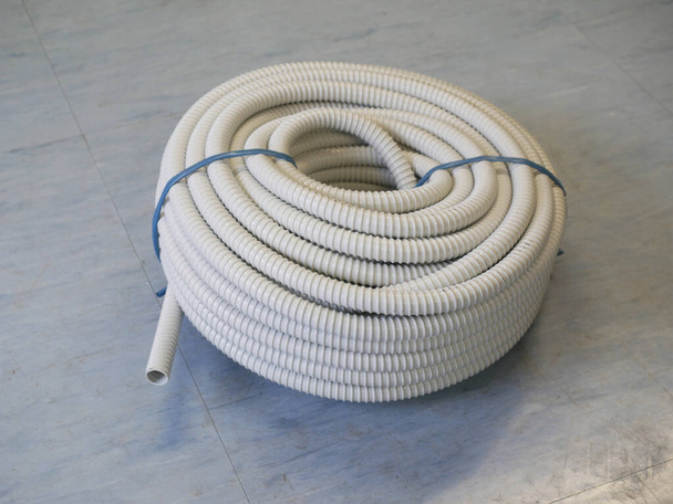 Rotolo di tubo flessibile ondulato in PVC grigio su pavimento azzurro - Foto, immagini
