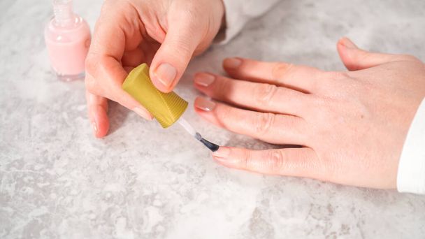 Женщина заканчивает маникюр дома простыми маникюрами. Картина ногтей со свежим лаком для ногтей. - Фото, изображение