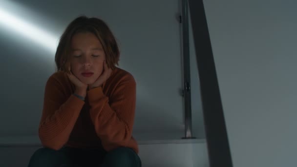 Smutna 12-letnia nastolatka siedzi z rozmysłem na schodach domu, odkładając głowę w dłoniach, odzwierciedlając problemy psychologiczne i samotność w okresie dojrzewania - Materiał filmowy, wideo