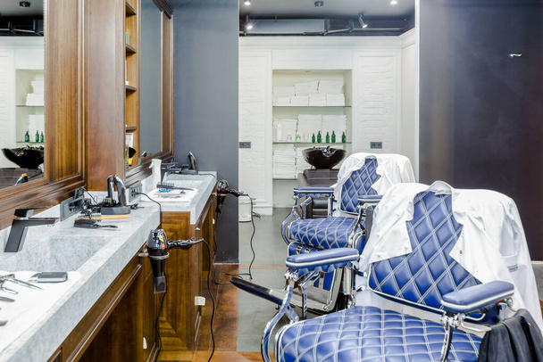 salon de coiffure de luxe intérieur, mobilier bleu cher, garniture en bois, plafond noir à la mode, robes blanches sur le dos des fauteuils - Photo, image