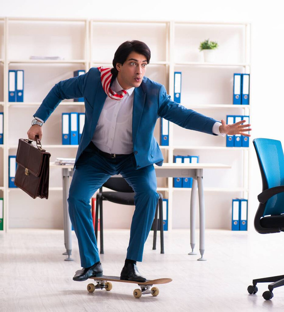 Il giovane bell'uomo d'affari con longboard in ufficio - Foto, immagini