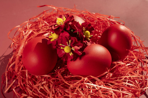 Colored eggs symbolize Easter in shades of red on straw - Fotografie, Obrázek