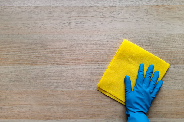 Scrub-a-Dub. Copy space. Top view. Concept of daily cleaning, washing, housework. Hand in blue rubber glove gets down to business, scrubbing wooden table with yellow rag. Flat lay. Place for text. - Photo, Image