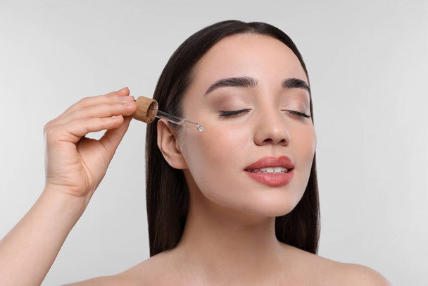 Young woman applying essential oil onto face on white background, closeup - Φωτογραφία, εικόνα