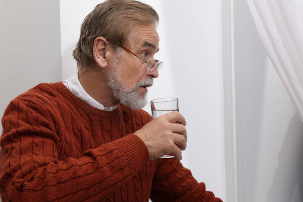 Upset senior man with glass of water at home Loneliness concept - Foto, afbeelding