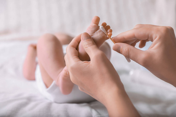 Mother cleaning baby's foot with cotton bud on bed, closeup - Foto, Imagem