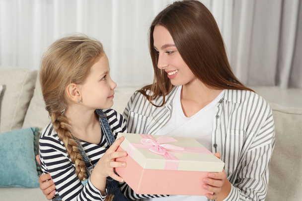 Cute little girl presenting her mother with gift on sofa at home - Fotografie, Obrázek