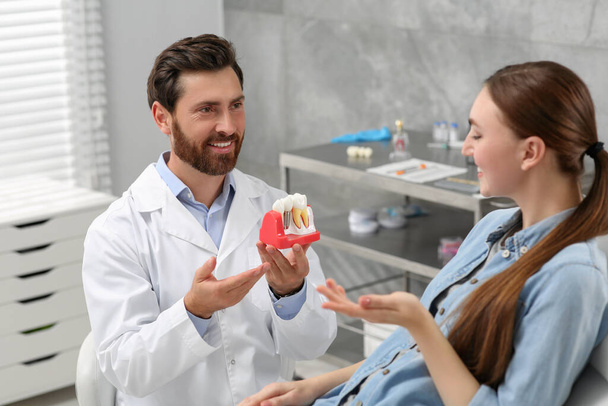 Doctor with educational model of dental implant consulting patient in clinic - Foto, Imagen