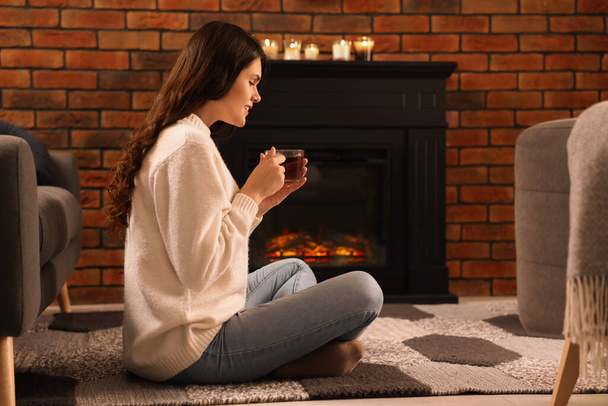 Young woman with cup of tea relaxing on floor near fireplace at home - Valokuva, kuva