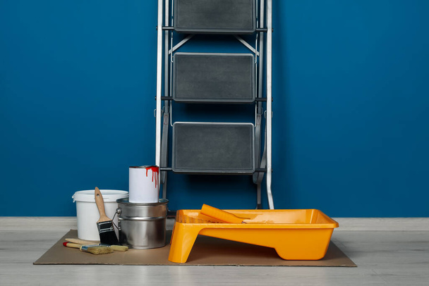 Metallic folding ladder and painting tools near blue wall indoors - Photo, Image
