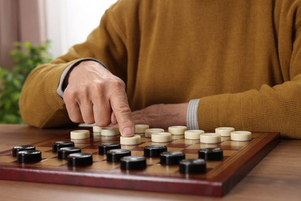 Playing checkers. Senior man thinking about next move at table in room, closeup - Foto, imagen