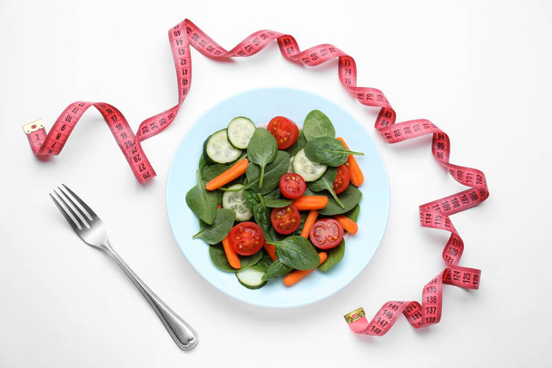 Maßband, Salat und Gabel auf weißem Hintergrund, flach gelegt - Foto, Bild
