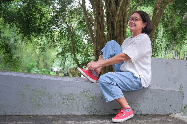 Asian woman sitting alone in the park, fixing her shoe lace, after a long walk - Photo, Image