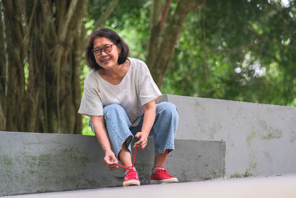 Asian woman sitting alone in the park, fixing her shoe lace, after a long walk - Foto, Imagen
