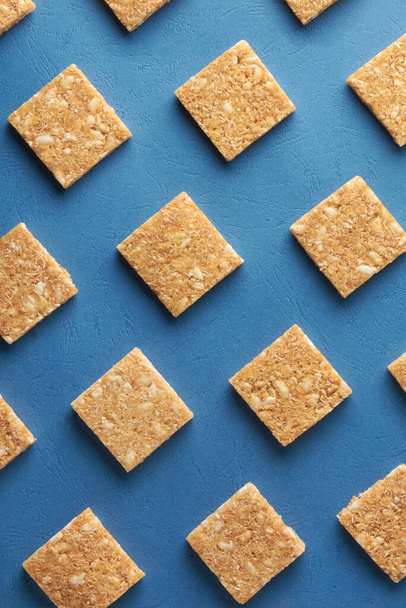 coconut biscuits pattern, crispy square shaped homemade cookies on textured blue surface, flat lay food background - 写真・画像