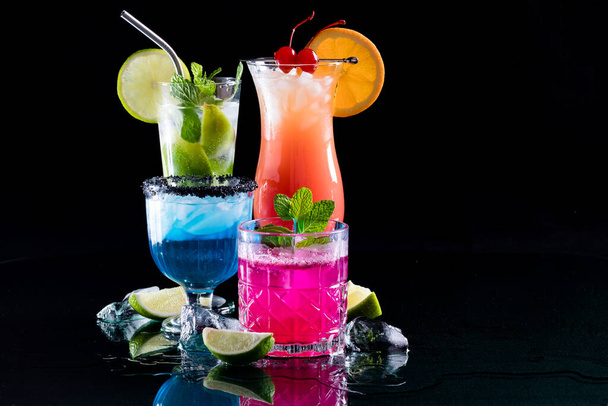 Een groep felgekleurde cocktails op reflecterend glas, tegen een zwarte achtergrond.  - Foto, afbeelding
