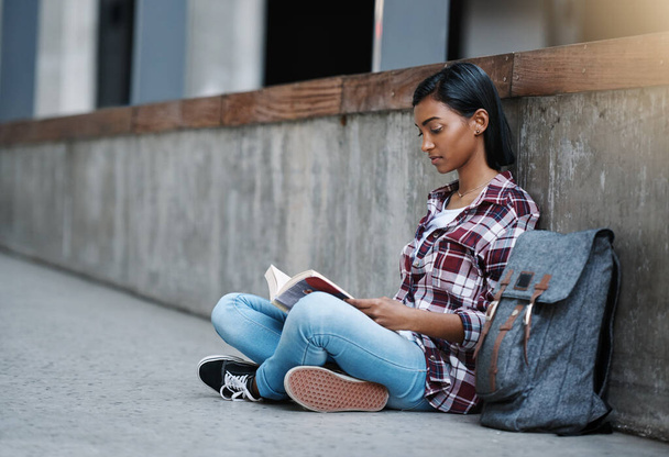 Si tiene occupata tra una lezione e l'altra. Scatto completo di una giovane studentessa attraente che legge un libro mentre è seduta fuori nel campus - Foto, immagini