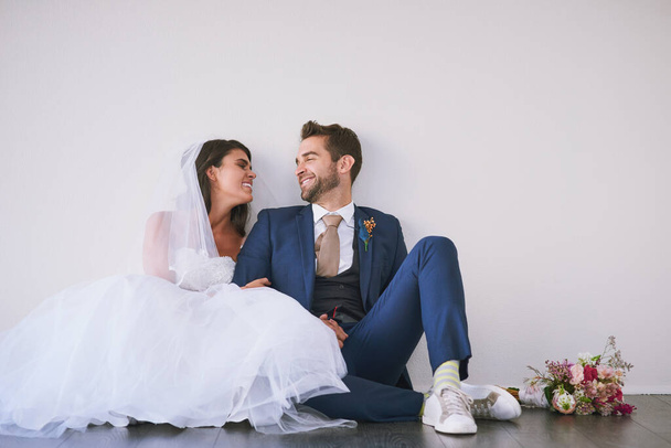 De liefde regeerde van de eerste date tot de I dos. Studio shot van een pas getrouwd jong paar zitten samen op de vloer tegen een grijze achtergrond - Foto, afbeelding
