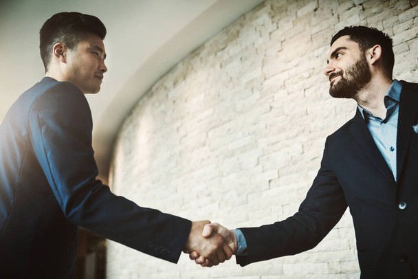The networking pros. two young businessmen shaking hands in a modern office - Foto, imagen