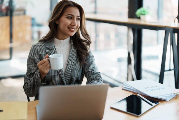 Πορτρέτο μιας επιχειρηματία που μιλάει στον υπολογιστή και πίνει καφέ. - Φωτογραφία, εικόνα