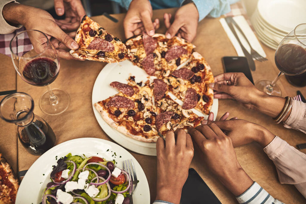 Yumulun. Bir grup tanınmayan insanın yüksek açılı görüntüsü. Her biri bir restoranda otururken bir dilim pizza alıyor. - Fotoğraf, Görsel