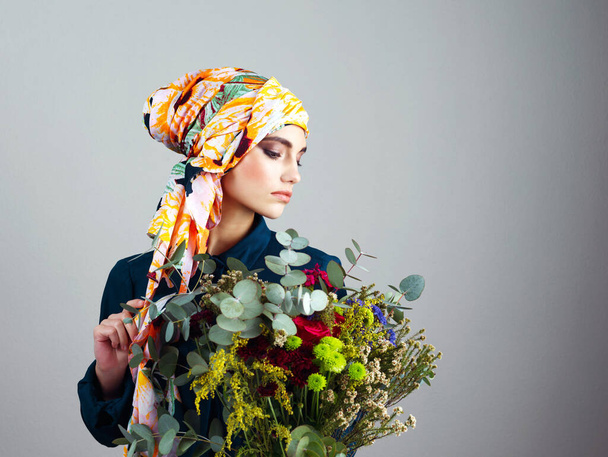 Будьте чесними, будьте квітами. Студійний знімок впевненої молодої жінки в барвистому шарфі голови і тримає букет квітів на сірому фоні
 - Фото, зображення
