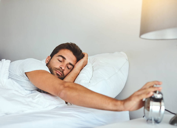 Еще пять минут. уставший молодой человек спит в своей постели, выключая будильник - Фото, изображение