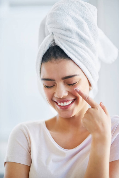 La piel nutrida brilla maravillosamente. una hermosa mujer joven aplicando crema hidratante en su piel en el baño en casa - Foto, Imagen