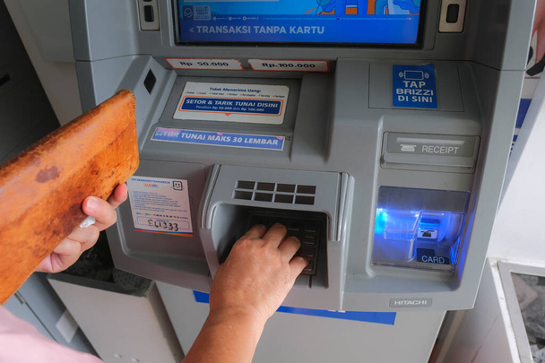 hands holding leather wallet, withdrawing some cash from ATM in Yogyakarta, 5 February 2023 - 写真・画像