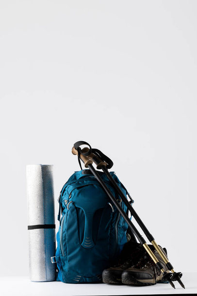 Close up of blue backpack, mat, trekking shoes and sticks on white background with copy space. National camping month, equipment and celebration concept. - Fotoğraf, Görsel