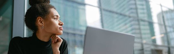 Libero professionista femminile che lavora su computer portatile mentre si siede in caffè e guarda su finestra. Foto di alta qualità - Foto, immagini
