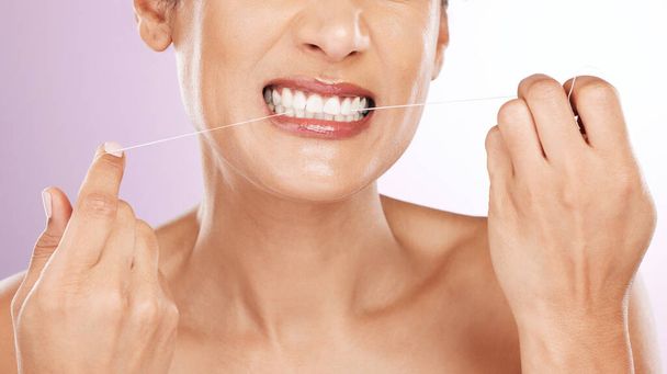 紫色の背景に隔離されたスタジオでの掃除、衛生、または歯のケアのための顔、女性と流れる歯。口腔健康、新鮮な息や健康のための歯科フロスやスレッドを持つ成熟した女性モデル. - 写真・画像