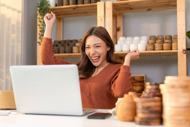 Entrepreneur of beautiful business asian young woman selling vase flower online with laptop and celebrating at home with her work success cheerful and happiness. Small Business Startup concept - 写真・画像