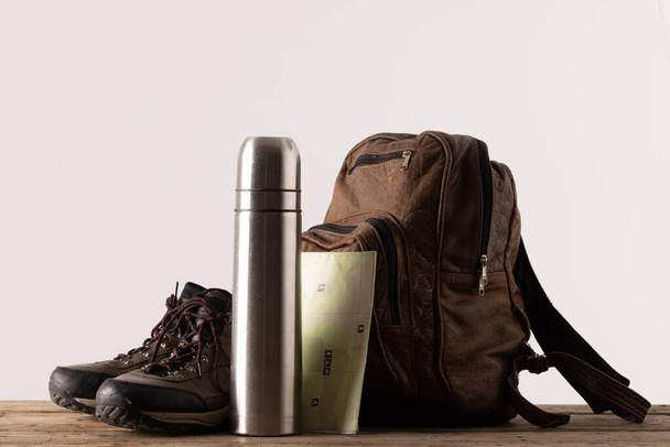 Close up of backpack, trekking shoes and thermos on table on white background with copy space. National camping month, equipment and celebration concept. - Φωτογραφία, εικόνα