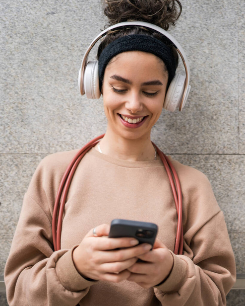 1人の女性若い大人世代z caucasian現代女性とともにヘッドフォンとスキップロープ幸せな笑顔使用携帯電話アプリトレーニングや音楽のためにオンラインで閲覧市内の実際の人コピースペース - 写真・画像