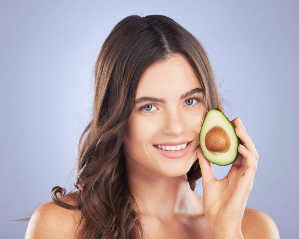 Woman, avocado and skincare in studio portrait with smile, organic cosmetics and nutrition for beauty. Girl, model and fruit for cosmetic, skin and natural healthy glow with pride by blue background. - Photo, Image