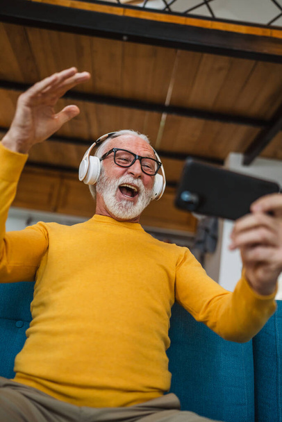 Ein älterer kaukasischer Mann sitzt zu Hause glücklich lächelnd Videospiele spielen Freizeitaktivität Spaß haben Handy Smartphone Spaß haben Kopierplatz - Foto, Bild