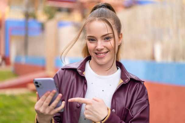 Junges hübsches Mädchen benutzt Handy im Freien mit traurigem Gesichtsausdruck - Foto, Bild