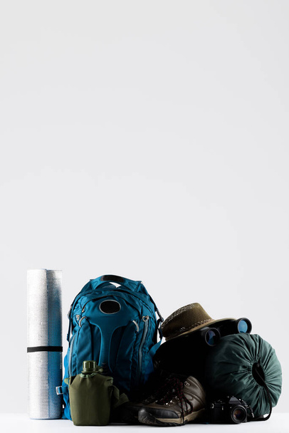 Close up of blue backpack, mat, trekking sticks and sleeping bag on white background with copy space. National camping month, equipment and celebration concept. - Zdjęcie, obraz