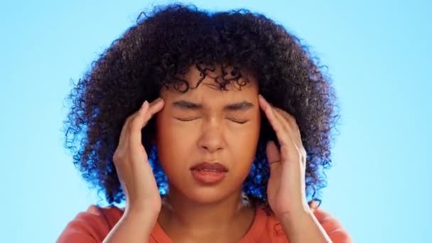 Black woman has headache, pain with stress and massage temple with hands on blue background. Female in studio, agony and suffering with anxiety and crisis, burnout and stressed about life problem. - Footage, Video