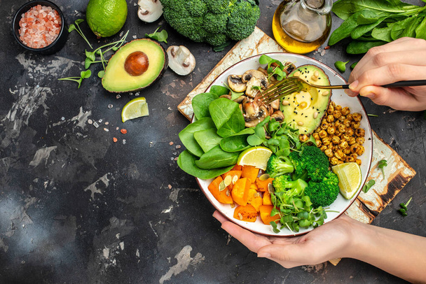 Meisje met bord en handen veganistisch ontbijt. maaltijd in kom met avocado, champignons, broccoli, spinazie, kikkererwten, pompoen. bovenaanzicht. - Foto, afbeelding