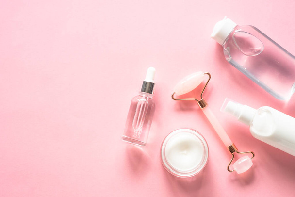 Skin care concept. Jade roller, cream and serum bottle on pink. Flat lay image with copy space. - Photo, Image