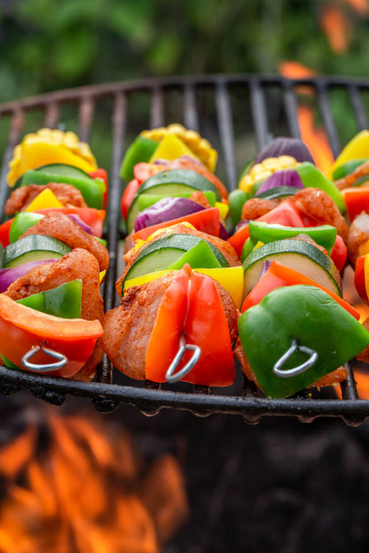 Hot and tasty skewers on grill with meat and vegetables. Skewers on fire made of fresh ingredients. - Foto, imagen