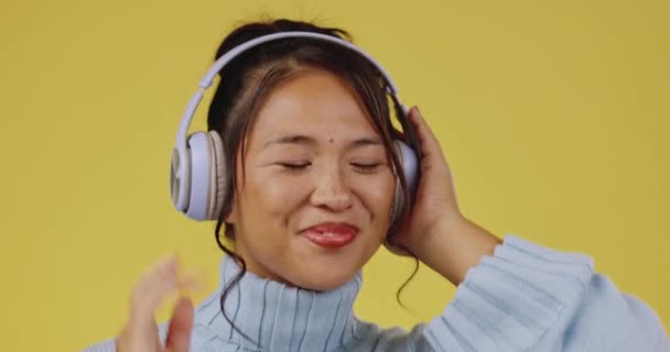 Fejhallgató, ázsiai nő és stúdió egy fiatal nővel, aki zenét hallgat és táncol. Boldogság, elszigetelt és sárga háttér egy gen z személy mosoly hallás és streaming rádió és dal. - Felvétel, videó