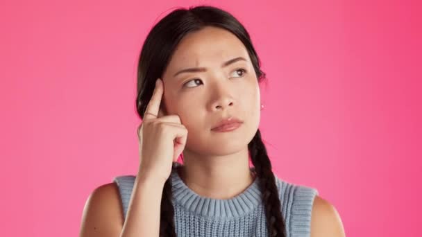 Asian woman, confused or thinking face on isolated studio background of skincare, beauty or makeup choice. Doubt, model or finger with ideas, questions or choosing vision in mind change on pink. - Footage, Video