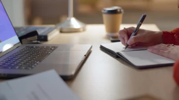 Γυναίκα, laptop και τα χέρια γράφοντας στο σημειωματάριο για το σχεδιασμό, το χρονοδιάγραμμα ή την επιχειρηματική υπενθύμιση στο γραφείο. Χέρι του εργαζομένου γυναίκα κρατώντας σημειώσεις στο βιβλίο ή ημερολόγιο από τον υπολογιστή στο τραπέζι για το σχέδιο του έργου. - Πλάνα, βίντεο